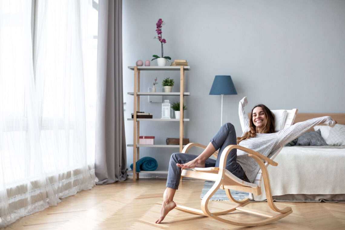 Glückliche Frau, die bequem auf einem modernen Stuhl im Wohnzimmer zu Hause sitzt, Sympboly für Lebensstil / Lifestyle.