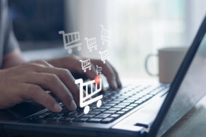 Person verwendet einen Computer-Laptop, um Online-Einkäufe auf virtuellen Bildschirmen eines Einkaufswagens zu bestellen.